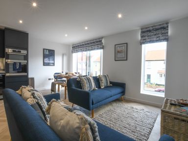 A living room with blue sofas and a dining table near windows at Salt Marsh House Southwold