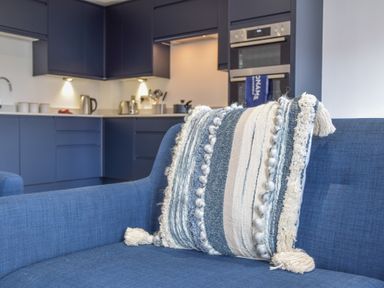 A blue sofa with a striped textured cushion in a kitchen with blue cabinets and built-in oven at Salt Marsh House Southwold