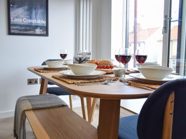 A dining table set with bowls plates wine glasses and bread next to a window at Salt Marsh House Southwold