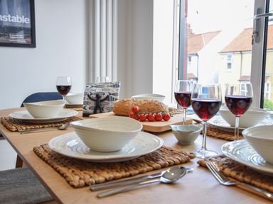 A dining table set with white bowls and plates red wine glasses bread and cherry tomatoes at Salt Marsh House Southwold