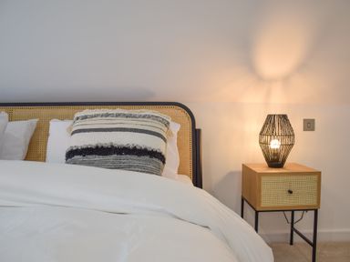 A bed with a woven headboard a striped pillow white bedding and a wooden bedside table with a lamp at Salt Marsh House Southwold