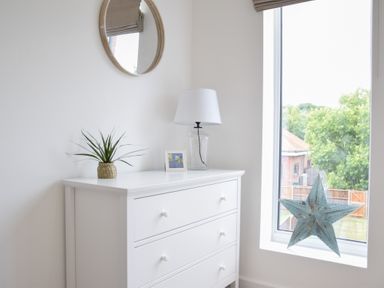 A white dresser with a lamp plant and picture frame near a window with a star decoration at Salt Marsh House Southwold