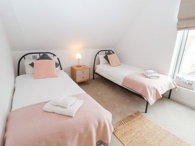 A bedroom with two beds, a nightstand, and a window at Salt Marsh House, Southwold