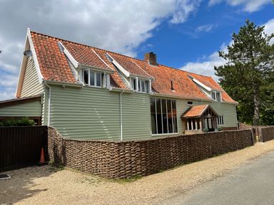 A light green house with a red tile roof and woven wooden fencing along the roadside at Moat Barn in Hasketon Near Woodbridge