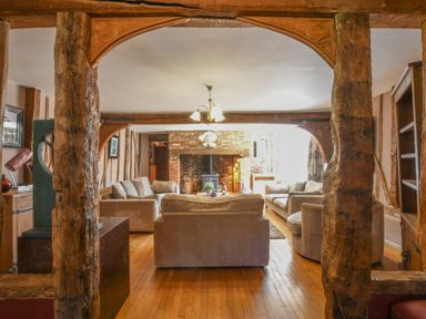 A living room with sofas around a brick fireplace and wooden beams at Moat Barn in Hasketon Near Woodbridge