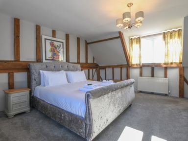 A bedroom with a large bed bedside table wooden beams and a window with curtains at Moat Barn Hasketon Near Woodbridge