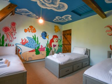 A bedroom with three single beds and under-bed drawers walls and ceiling painted with underwater cartoon characters at Moat Barn in Hasketon Near Woodbridge