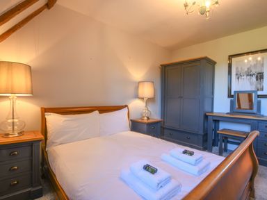 A bedroom with a wooden bed white linens two lamps a dark wardrobe and a dressing table at Moat Barn in Hasketon Near Woodbridge