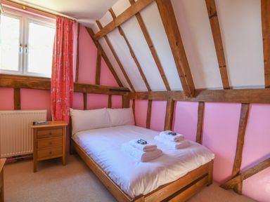 A bedroom with a double bed wooden side table and pink walls at Moat Barn Hasketon Near Woodbridge