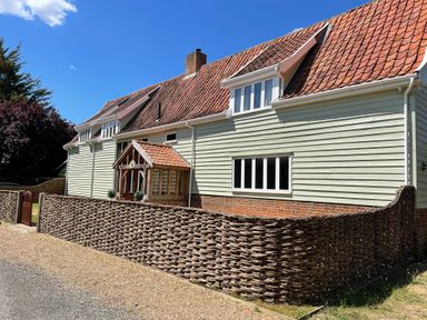 A house with a tiled roof wooden porch and woven fence on a gravel path at Moat Barn in Hasketon Near Woodbridge