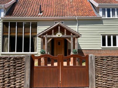 A wooden gate and woven fence in front of a house entrance with a wooden porch at Moat Barn Hasketon Near Woodbridge