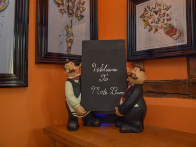 Two figurines holding a sign that reads Welcome To Moat Barn with framed butterfly artwork on the wall at Moat Barn Hasketon Near Woodbridge