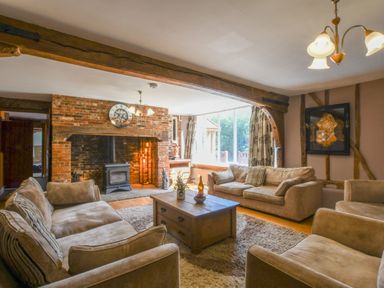 A living room with beige sofas a wooden coffee table a brick fireplace and a large window at Moat Barn in Hasketon Near Woodbridge