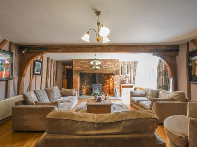 A living room with beige sofas around a wooden coffee table and a brick fireplace at Moat Barn in Hasketon Near Woodbridge