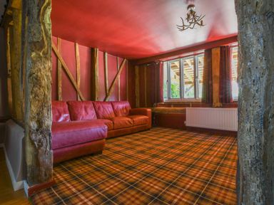 A lounge with a red leather sectional sofa and a plaid carpet at Moat Barn in Hasketon Near Woodbridge