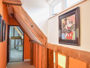 A hallway with orange walls wooden beams and a framed picture of Mickey Mouse at Moat Barn Hasketon Near Woodbridge