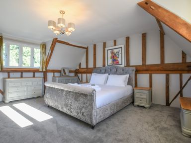 A bedroom with a large bed white linens wooden beams gray carpet and multiple dressers at Moat Barn in Hasketon Near Woodbridge