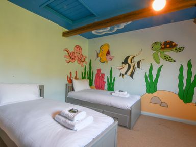A childrens bedroom with two single beds and painted sea creatures on the wall at Moat Barn in Hasketon Near Woodbridge