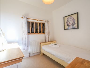 A bedroom with a single bed a desk a window with curtains and a framed picture on the wall at Moat Barn in Hasketon Near Woodbridge