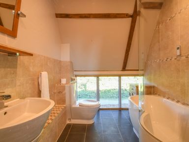 A bathroom with a sink a toilet and a bathtub under a sloped ceiling with wooden beams at Moat Barn Hasketon Near Woodbridge