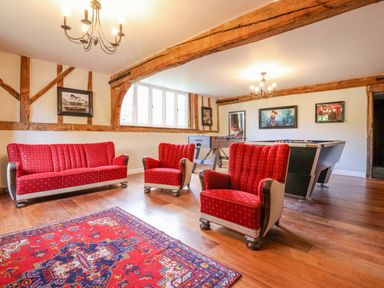 A game room with red upholstered sofa and chairs a foosball table and a pool table with wooden beams on the walls and ceiling at Moat Barn Hasketon Near Woodbridge
