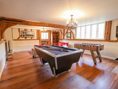 A game room with a pool table foosball table red sofa and wooden beams at Moat Barn in Hasketon Near Woodbridge