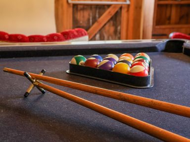 A pool table with billiard balls in a triangle rack and two wooden pool cues crossed at Moat Barn in Hasketon Near Woodbridge