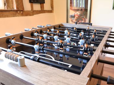 A foosball table with player figures in a room with wooden beams and a framed picture on the wall at Moat Barn in Hasketon Near Woodbridge