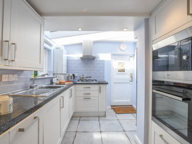 A kitchen with white cabinets a gas stove a sink and a microwave at 17 South Green Southwold