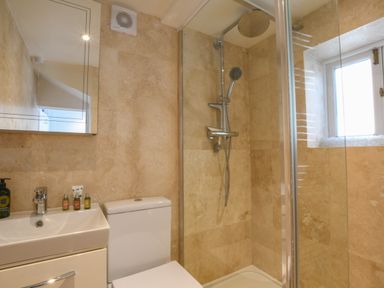 A bathroom with a sink cabinet a toilet and a walk-in shower with glass door and a window at 17 South Green Southwold