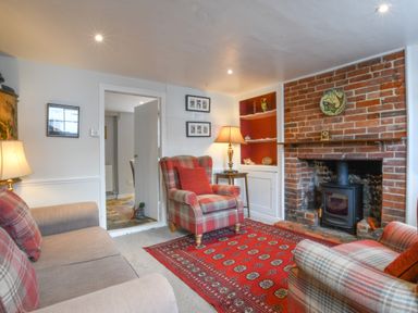 A living room with plaid armchairs a red patterned rug a brick fireplace and lamps at 17 South Green Southwold