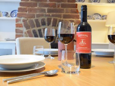 A dining table set with plates glasses silverware and a bottle of red wine in front of a brick fireplace at 17 South Green Southwold