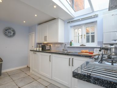A kitchen with white cabinets a black countertop a window above the sink and a gas stove at 17 South Green Southwold