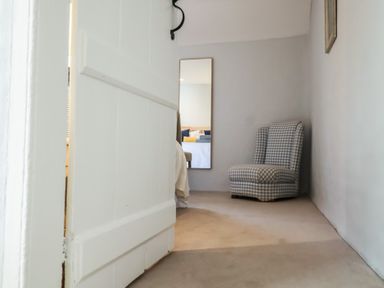 A room with a white door partially open a checked armchair and a mirror on the wall at 17 South Green Southwold