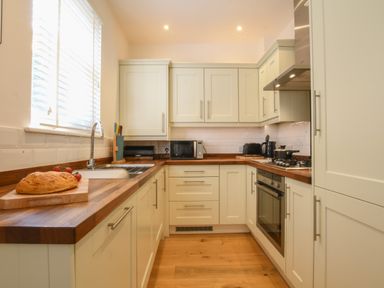 A kitchen with wooden countertops white cabinets a loaf of bread on a cutting board and appliances at The Gallery Blythburgh near Southwold