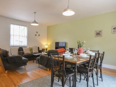 A dining table set with bowls and glasses next to a living room with sofas and a television at The Gallery, Blythburgh near Southwold