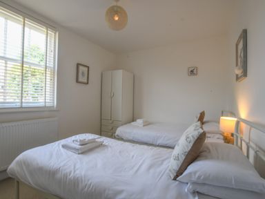 A bedroom with two single beds a white wardrobe and a window with blinds at The Gallery Blythburgh near Southwold