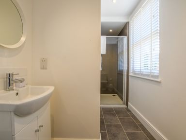 A bathroom with a sink cabinet and mirror and a shower enclosure with towel near window blinds at The Gallery Blythburgh near Southwold