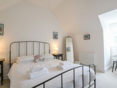 A bedroom with a metal bed frame white bedding folded towels bedside tables lamps a floor mirror and framed pictures at The Gallery Blythburgh near Southwold