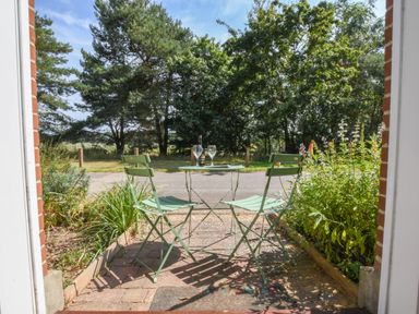 A small patio with green metal table and two chairs with wine glasses and bottle surrounded by plants and trees at The Gallery Blythburgh near Southwold