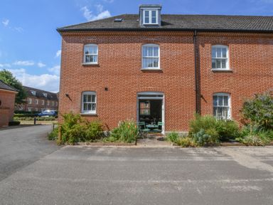 The front exterior of a brick building with windows and an open doorway leading to a patio with a table and chairs at The Gallery in Blythburgh near Southwold
