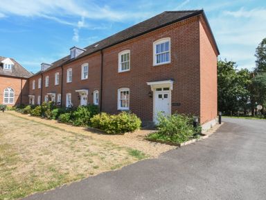 A row of attached brick houses with white doors and windows next to a gravel path and lawn at The Gallery Blythburgh near Southwold