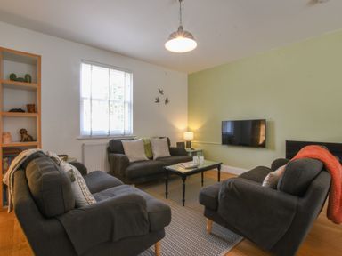 A living room with three dark sofas a coffee table a wall-mounted TV and a window at The Gallery, Blythburgh in Blythburgh near Southwold