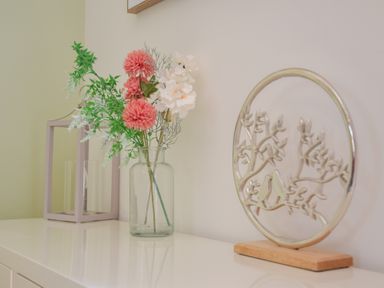 A glass vase with flowers and a decorative metal circle with birds on a branch on a white surface at The Gallery Blythburgh near Southwold