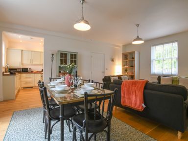 A dining area with a glass table set for six next to a living room with sofas and a window at The Gallery Blythburgh near Southwold