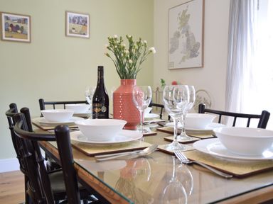 A dining table set with white bowls glasses cutlery a flower vase and a bottle of wine at The Gallery Blythburgh near Southwold