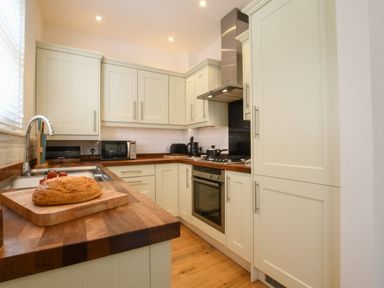 A kitchen with wooden countertops, white cabinets, a loaf of bread on a cutting board, a sink with a faucet, microwave, toaster, kettle, stove, and oven at The Gallery, Blythburgh in Blythburgh near Southwold