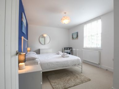 A bedroom with a white metal bed frame with folded towels on the bed and a round mirror on the wall at The Gallery, Blythburgh