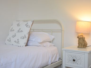 A bed with white bedding and a pillow with rabbit prints next to a nightstand with a lamp featuring a rabbit-shaped base at The Gallery Blythburgh near Southwold