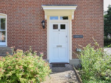 A front door of a brick house with plants on each side and a wall lamp at The Gallery 53 in Blythburgh near Southwold